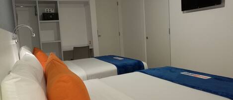 A hotel room with two beds, a TV mounted on the wall, a small kitchenette, and a wardrobe.