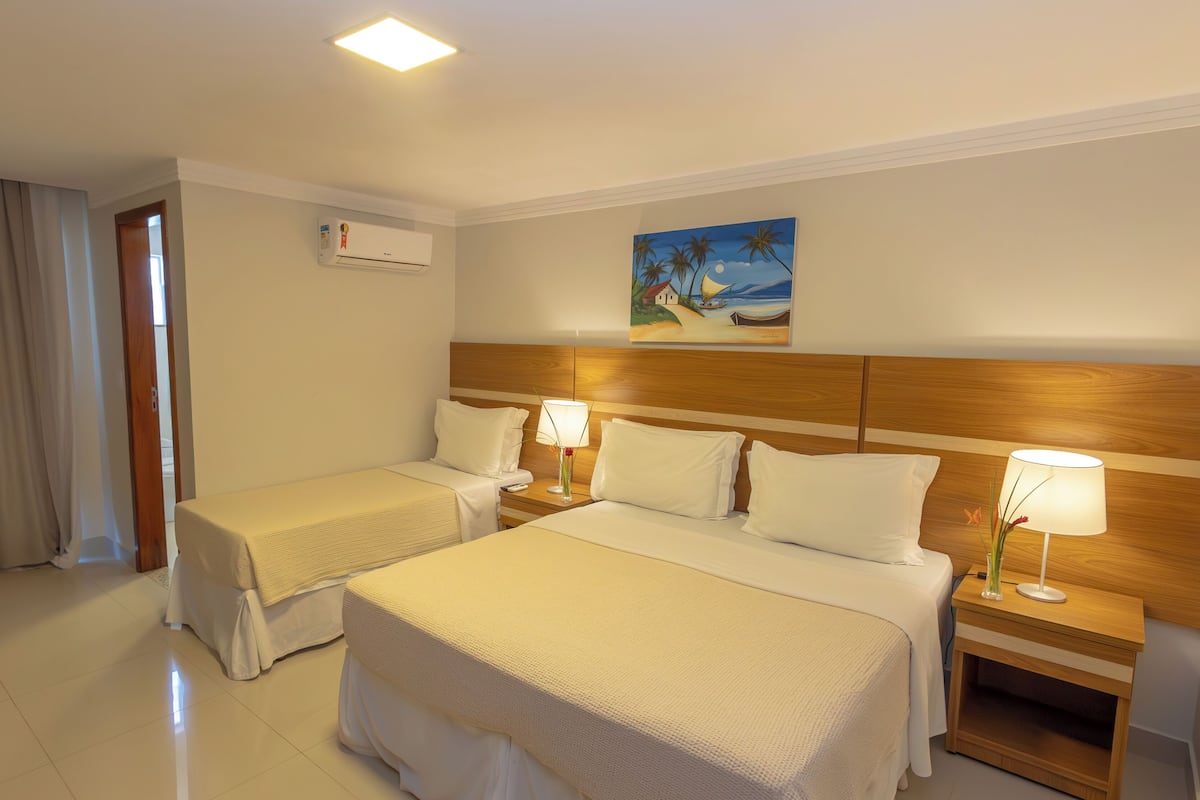 A hotel room with two beds, a wooden headboard, a painting of a beach scene, and a nightstand with a lamp.