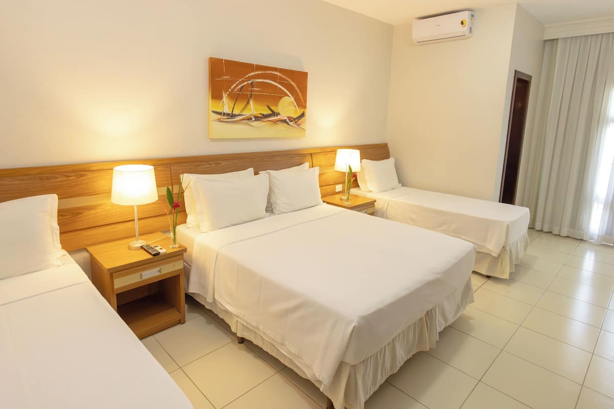 A hotel room with two beds, a nightstand with a lamp, a painting on the wall, and an air conditioning unit.