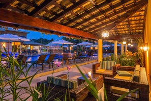 An outdoor seating area with wicker furniture and umbrellas, overlooking a pool. - Vitória Régia Hotel (Porto Seguro)