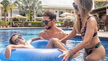 Une zone de piscine avec un flotteur gonflable bleu, des palmiers et un bâtiment doté d’une terrasse à l’arrière-plan.