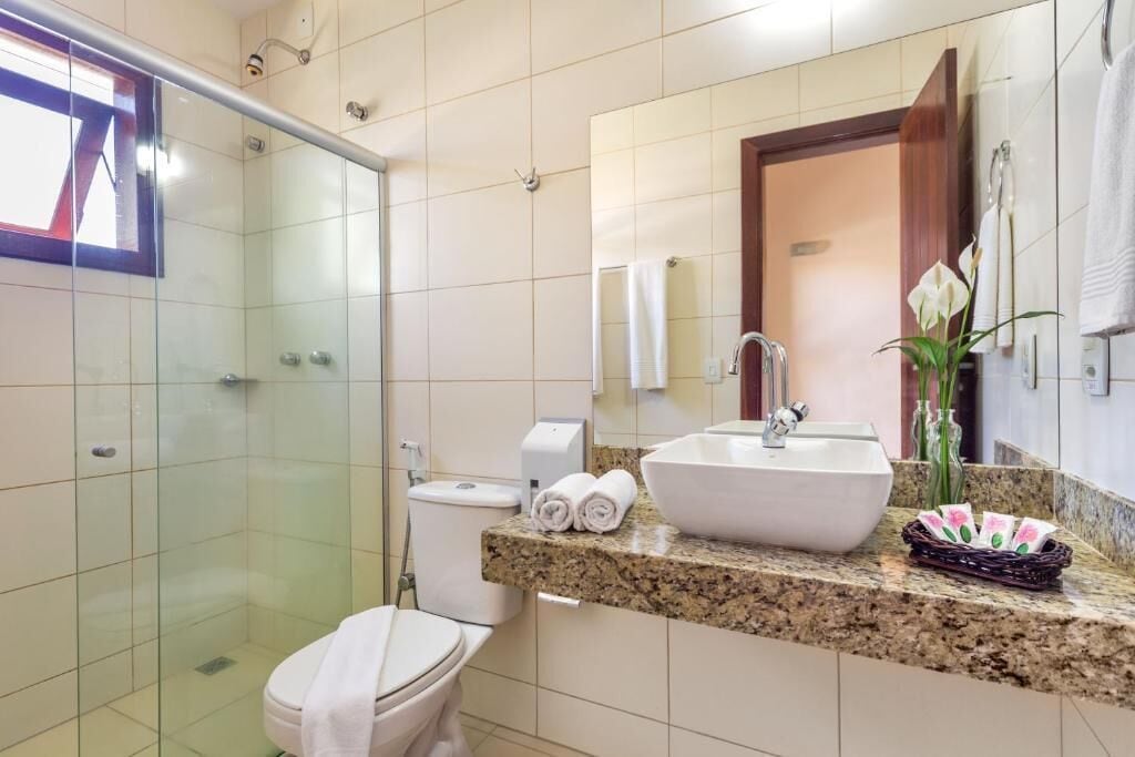 A modern bathroom with a glass shower enclosure, a white toilet, a large sink with a marble countertop, and a mirror above the sink.