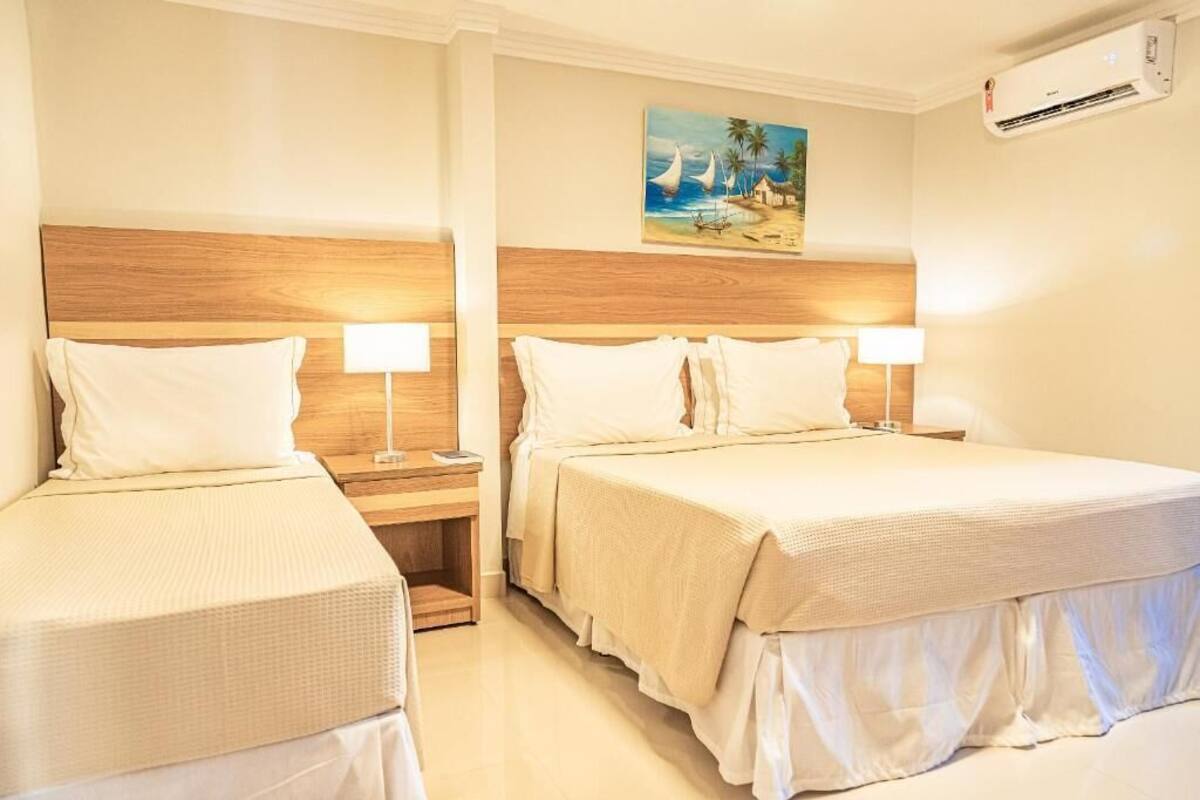 A hotel room with two beds, each with a wooden headboard, white bedding, and bedside lamps. There is a painting of a beach scene on the wall above the beds.