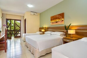 Een hotelkamer met twee bedden, een bureau en een raam met uitzicht op groen.