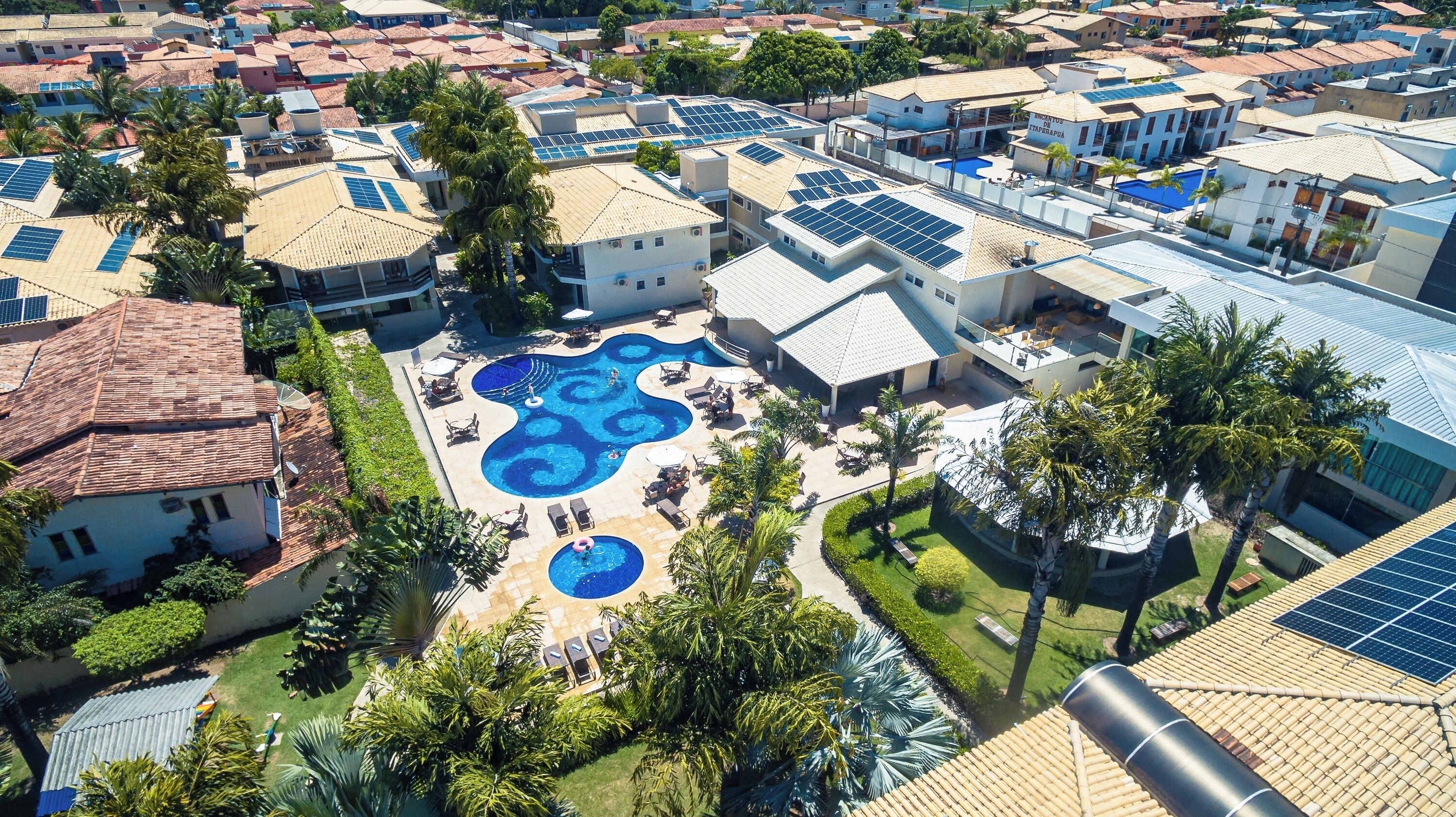 An aerial view of a residential area with multiple houses, a swimming pool, and solar panels on rooftops.
