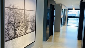 A hallway with a large framed picture of trees, a ceiling-mounted device, and a sign indicating a salon. - Hotel Kennedy (Sao Jose)