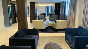 A modern hotel lobby with dark sofas, a central coffee table, and a view of the city through large windows. - Hotel Kennedy (Sao Jose)