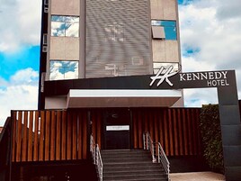Entrada do Hotel Kennedy, com fachada moderna, uma escadaria que leva à entrada e uma placa sobre a porta.