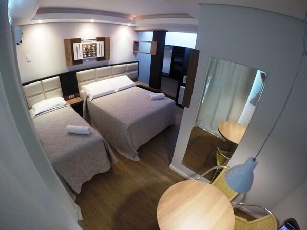 Hotellihuone, jossa on kaksi sänkyä, pieni työpöytä, tuoli, peili ja lamppu.