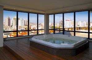 Una habitación moderna con ventanas amplias que ofrecen vistas a la ciudad, suelo de madera y una bañera de hidromasaje.