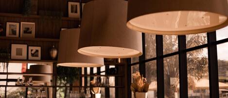 A bar area with hanging lamps, shelves with framed pictures, and a view of parked cars outside.