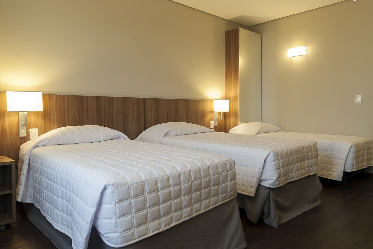 A hotel room with two beds, each with a headboard and bedside lamps.