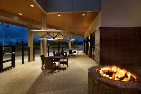 An outdoor patio area with tables and chairs, a fire pit, and umbrellas providing shade.