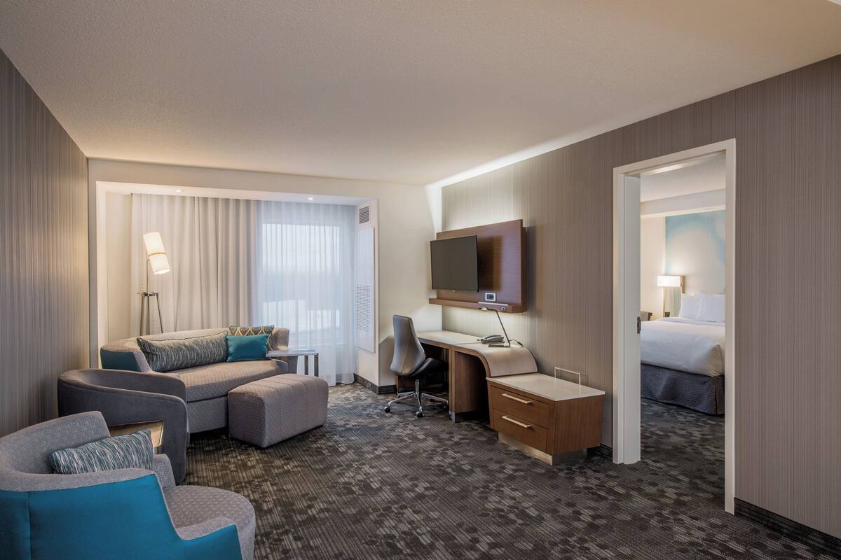 A hotel room with a sofa, a desk, a TV, and a bed.