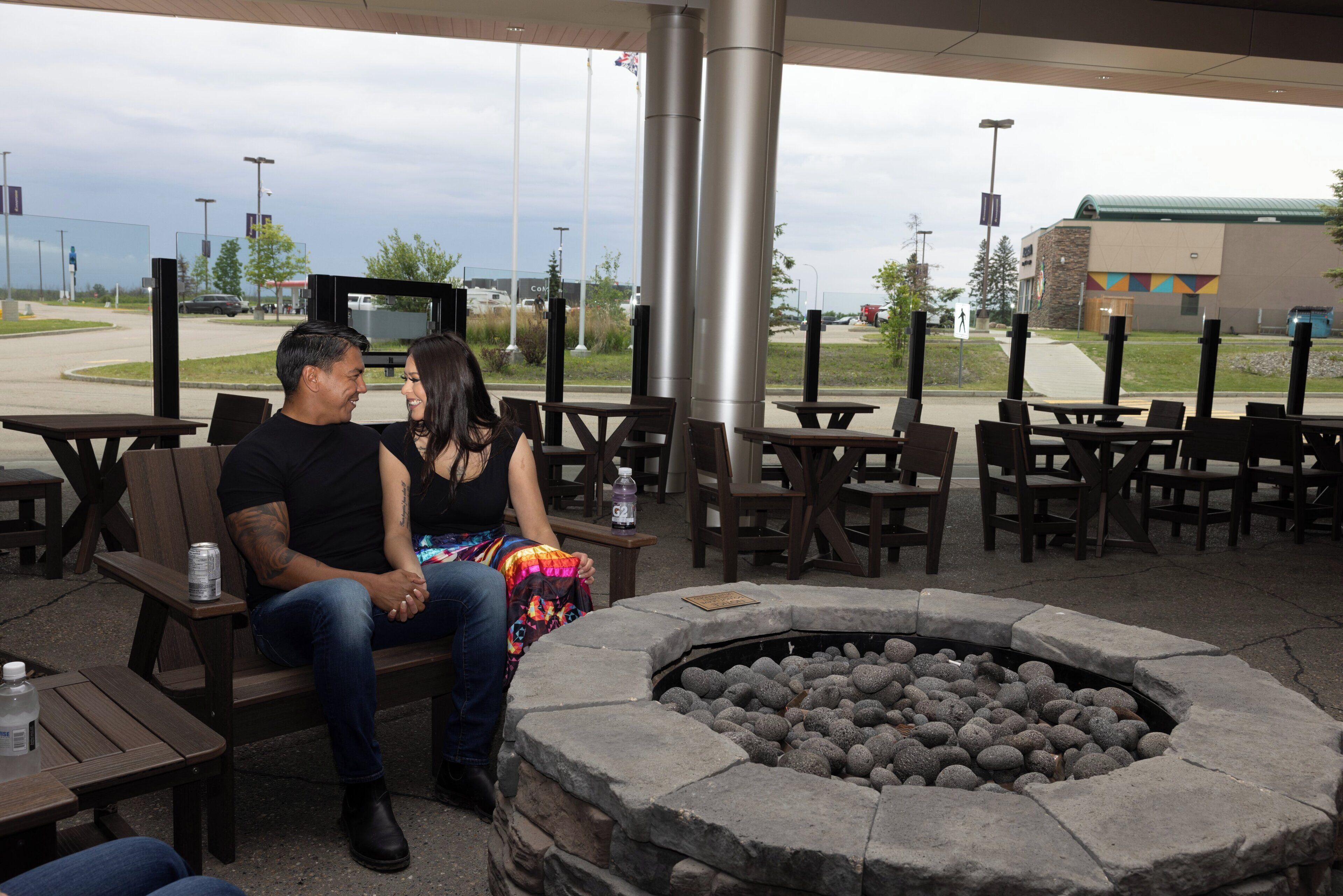 A couple seated at a wooden table with a stone fire pit in the foreground.