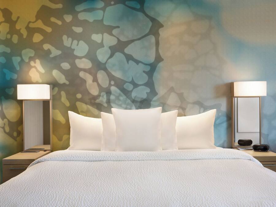 A hotel room with a large bed, two bedside tables, and a wall with a textured abstract design.