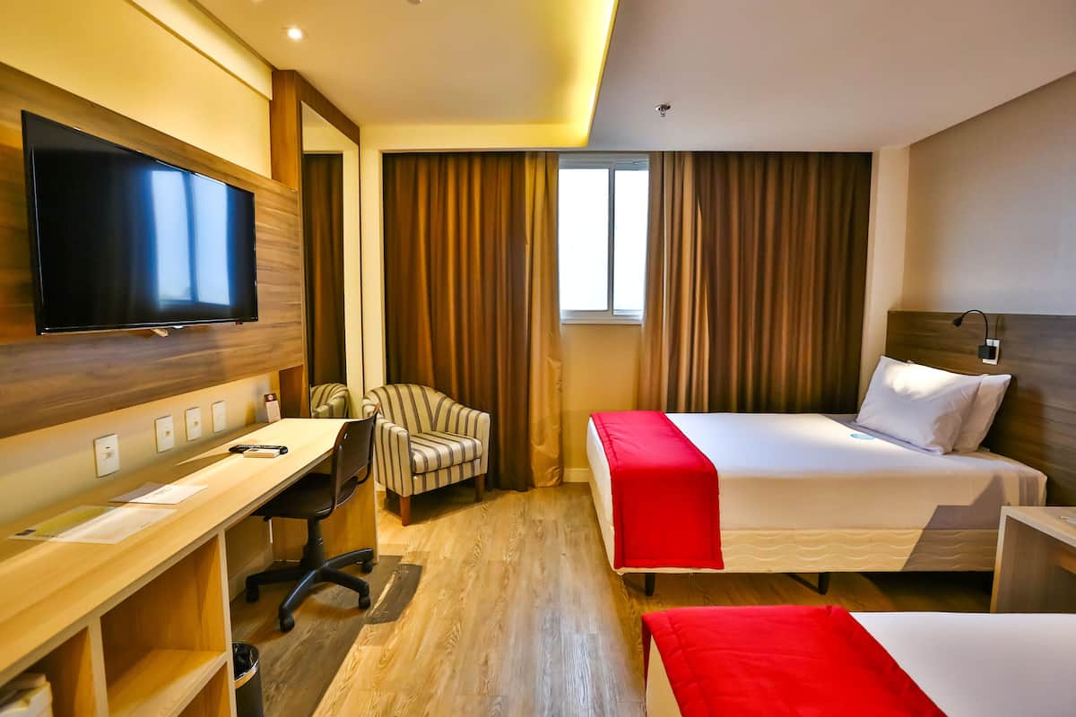 Ein Hotelzimmer mit Bett, Schreibtisch, Stuhl, Fernseher und Vorhängen.