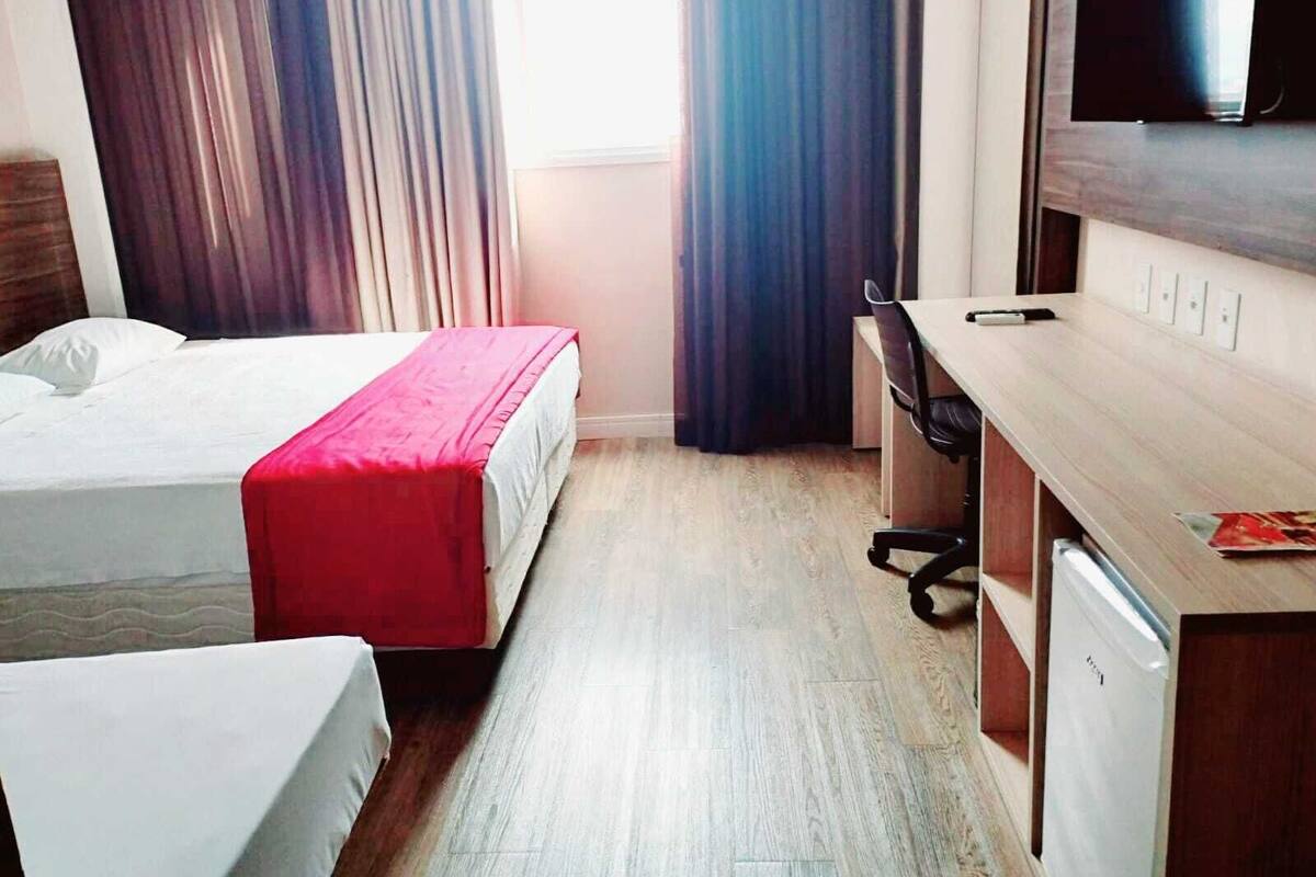 Ein Hotelzimmer mit zwei Betten, einem Schreibtisch, einem Stuhl, einem Fernseher und einem Fenster mit Vorhängen.