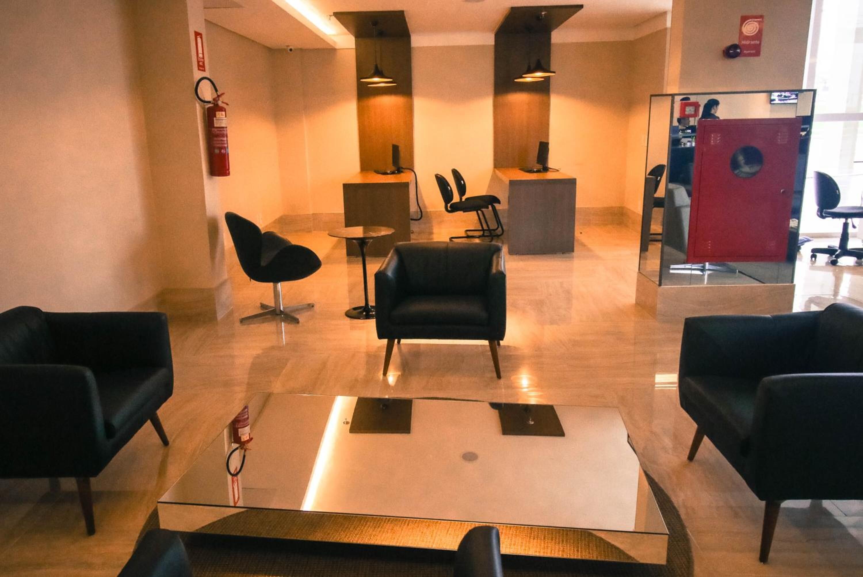 Un hall d’entrée moderne avec des fauteuils en cuir noir, une table basse en verre et un comptoir d’accueil.