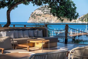 A seaside lounge with a sofa, chairs, and a wooden table. A rope barrier separates the seating area from the water. - Wyndham Datca Perili Bay (Datça)