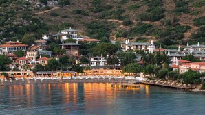 A coastal town with buildings along the waterfront, a marina with boats, and a hillside backdrop. - Wyndham Datca Perili Bay (Datça)