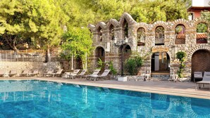 A pool with clear blue water, surrounded by stone walls and lounge chairs. - Wyndham Datca Perili Bay (Datça)