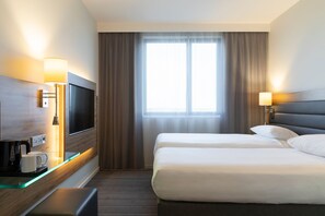 A hotel room with a bed, a TV, a bedside table with a lamp, and a window with curtains. - Moxy Aberdeen Airport (Aberdeen)