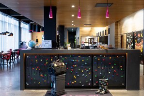 A modern reception area with a black wall featuring colorful letters and a luggage stand. - Moxy Aberdeen Airport (Aberdeen)