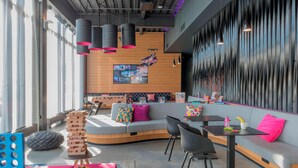 A modern lounge area with a curved sofa, black chairs, a small table, and a large window. - Moxy Aberdeen Airport (Aberdeen)