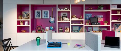 A modern workspace with a white table, two chairs, a typewriter, a laptop, and a striped ottoman.