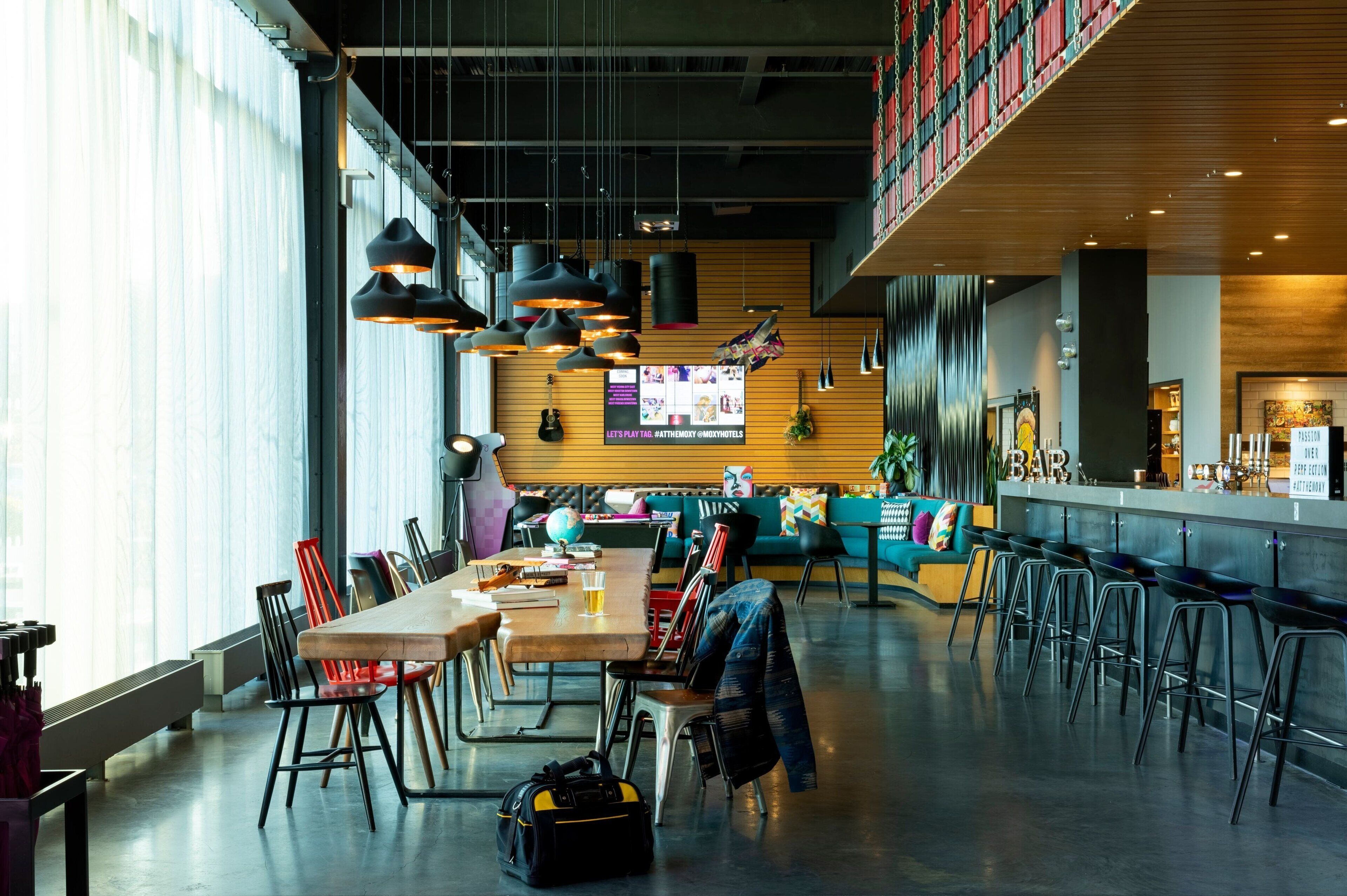 A modern interior with a long communal table, multiple bar stools, and a bar area.