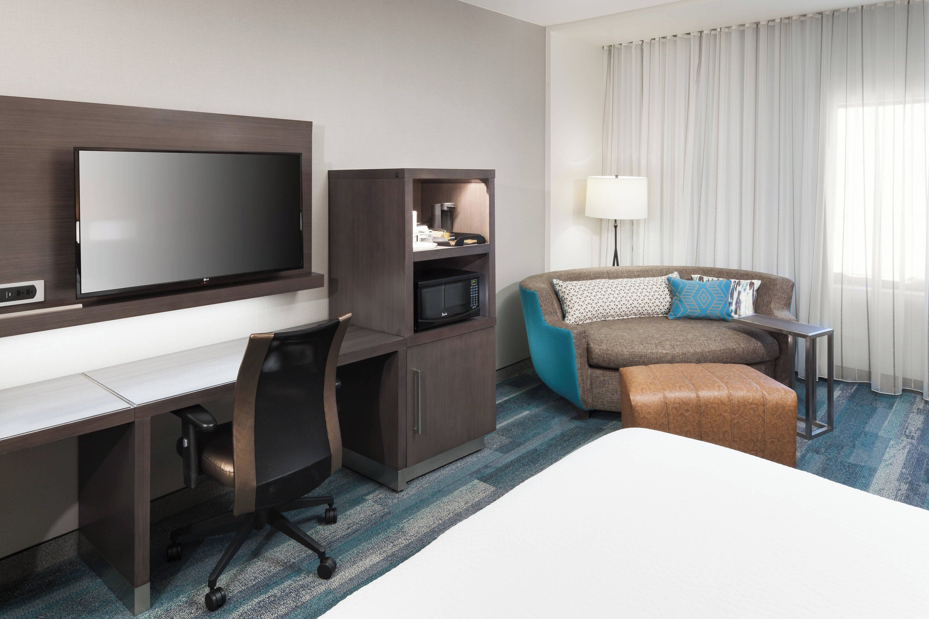 Habitación de hotel con cama, escritorio con televisor, kitchenette, sofá y lámpara.