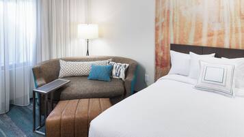 A hotel room with a bed, a sofa, a small table, and a lamp.