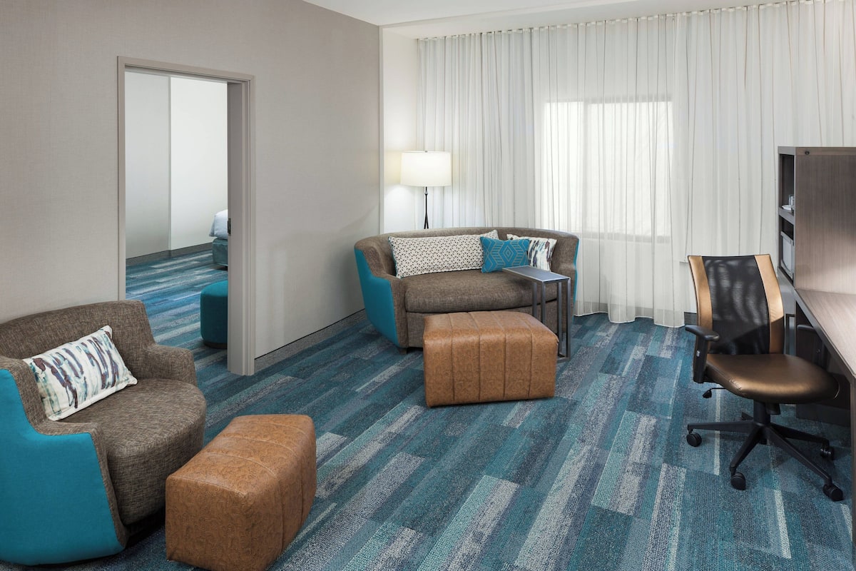 Ein Hotelzimmer mit einer Couch, einem Hocker, einem Schreibtisch und einem Sessel.