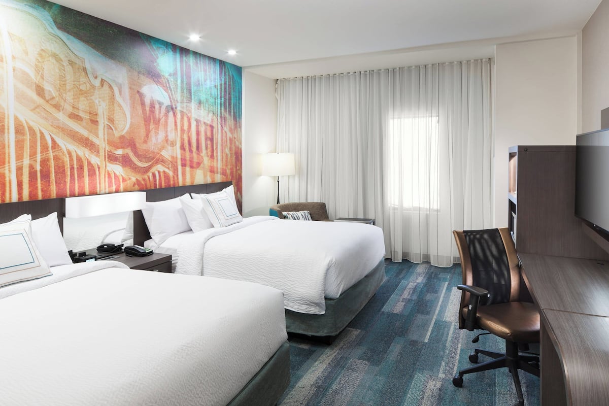 Ein Hotelzimmer mit zwei Betten, einem Schreibtisch, einem Stuhl, einem Fernseher und einem großen, abstrakten Gemälde an der Wand.