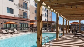 A pool area with lounge chairs and umbrellas, wooden pergola, and a building in the background.
