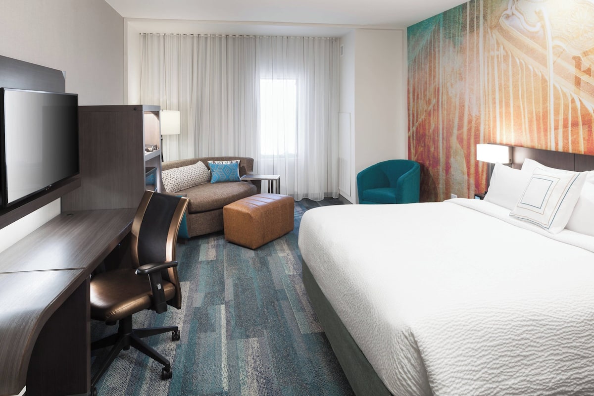 Ein Hotelzimmer mit Bett, Schreibtisch, Stuhl, Fernseher und einem großen Fenster mit Vorhängen.