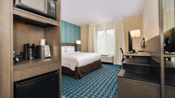 A hotel room with a bed, a desk with a lamp, a microwave, and a refrigerator.