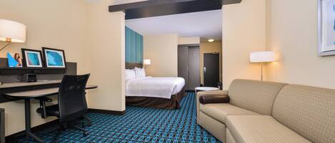 A hotel room with a bed, a desk with a chair, a sofa, and a patterned carpet.