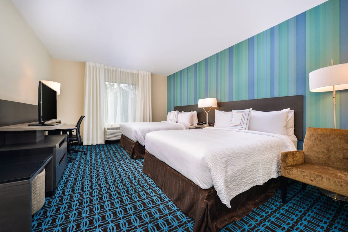 A hotel room with two beds, a desk, a TV, and a chair.