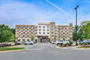 A multi-story Fairfield Inn & Suites hotel with a central entrance, parking lot, and surrounding greenery.