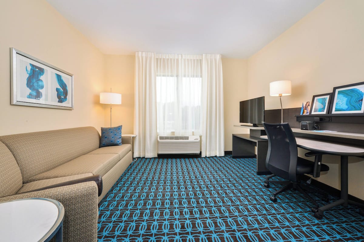 A hotel room with a sofa, a desk, a chair, a TV, and a lamp.