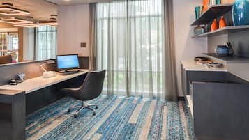 A hotel room with a desk, chair, computer, and a large window with curtains.