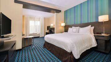 A hotel room with a large bed, a flat-screen TV, a desk with a chair, and a window with curtains.