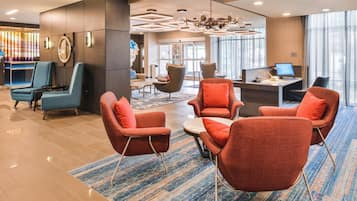 A modern lobby with a mix of seating options, including armchairs and a sofa, a reception desk, and a large chandelier.