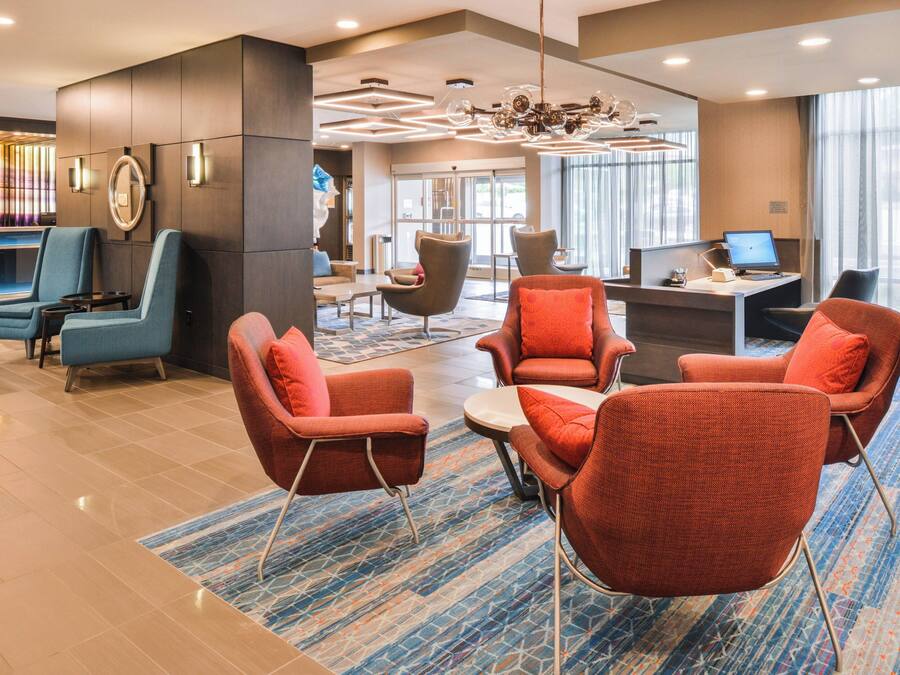 A modern lobby with a mix of seating options, including armchairs and a sofa, a reception desk, and a large chandelier.