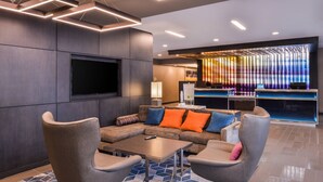 A modern lobby with a sectional sofa, armchairs, a flat-screen TV, a bar area, and a patterned rug. - Fairfield Inn & Suites by Marriott Raleigh Cary (Cary)
