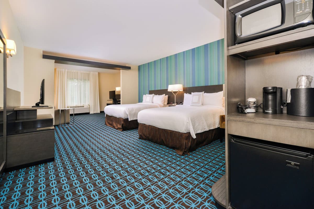 A hotel room with two beds, a kitchenette, a flat-screen TV, and a large window with curtains.