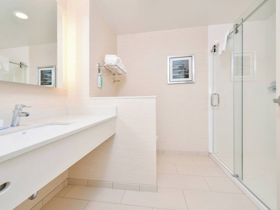 A modern bathroom with a white sink, a glass shower enclosure, and a framed picture on the wall.