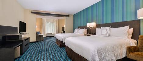 A hotel room with two beds, a desk with a TV, and a patterned carpet.